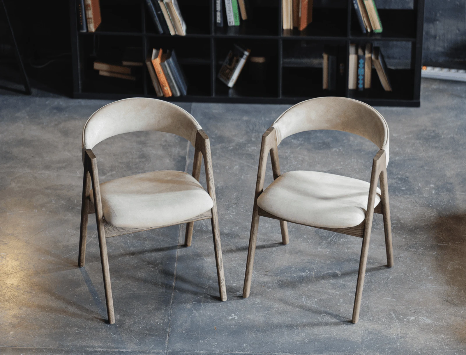 Light beige Bolzano Lain chairs in a library against shelves filled with books, natural-ash sawhorse frame