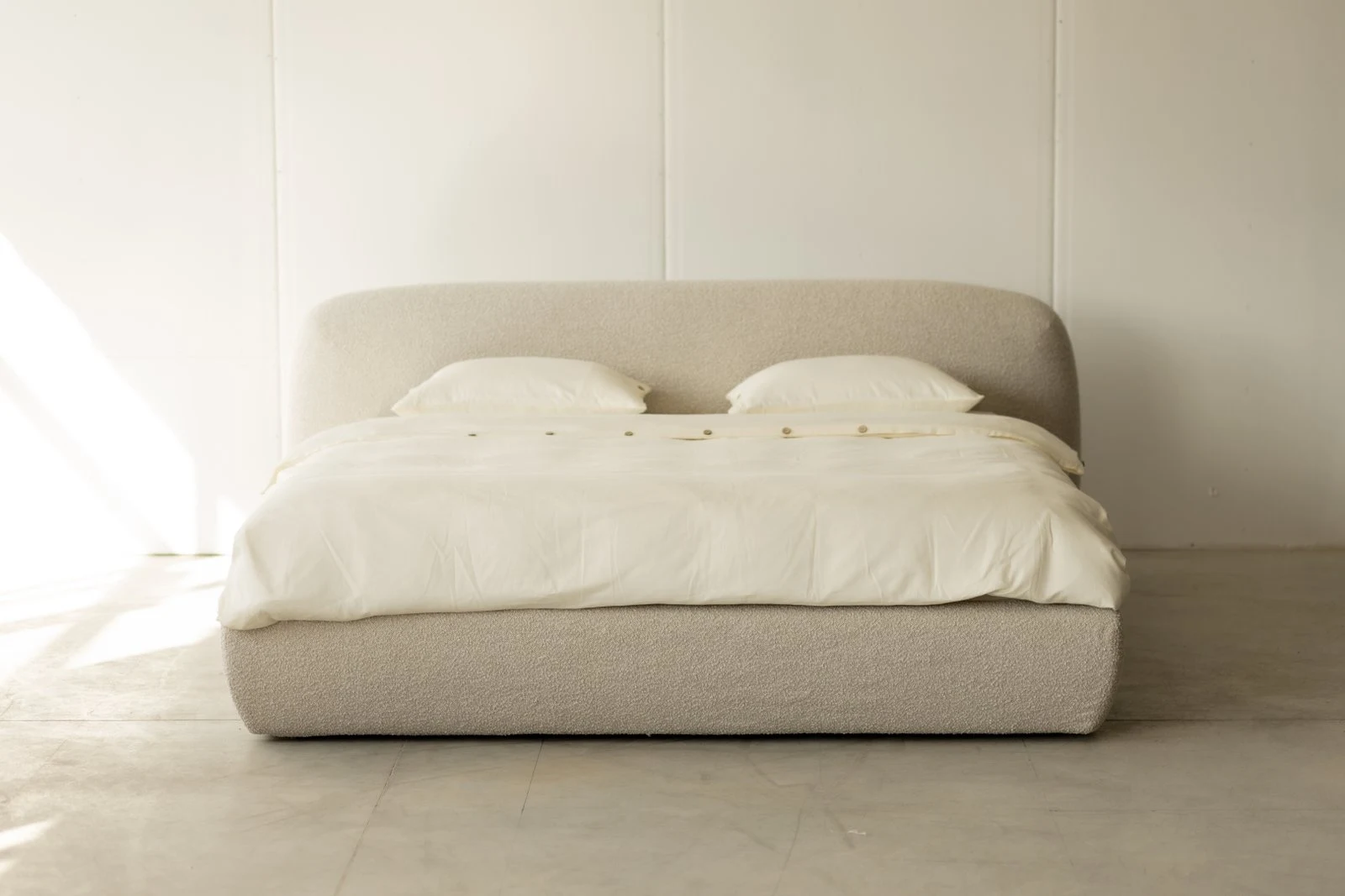 Cream boucle Belagio centered against a white panel-board wall, soft daylight from camera left