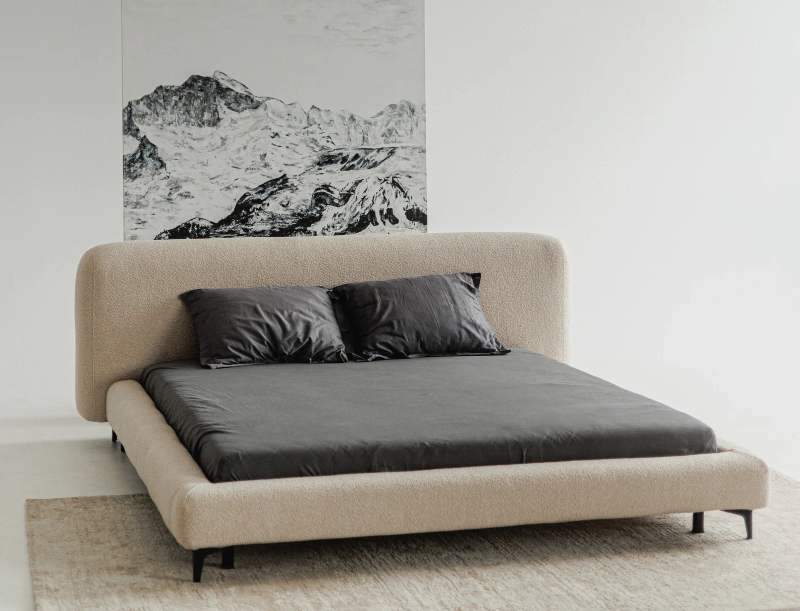 Three-quarter view of the sand Baloo 2074 boucle Fresco bed showing the arched headboard form against the black-and-white mountain artwork