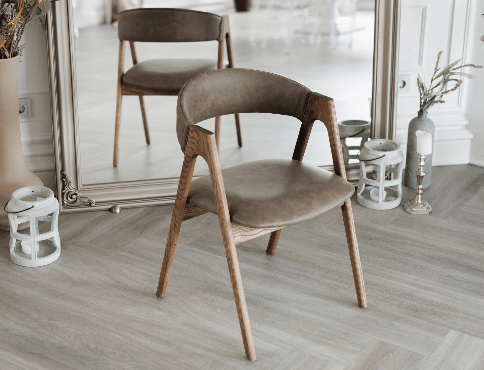 A coffee-brown leather Lain chair on natural-ash frame beside a tall gold-framed mirror, candles and lanterns nearby