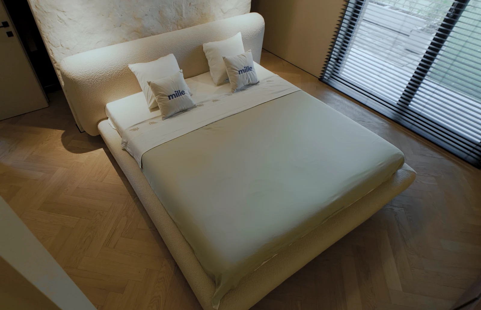Cream Copenhagen 900 boucle Fresco bed photographed from above against a textured plaster wall with herringbone parquet floor