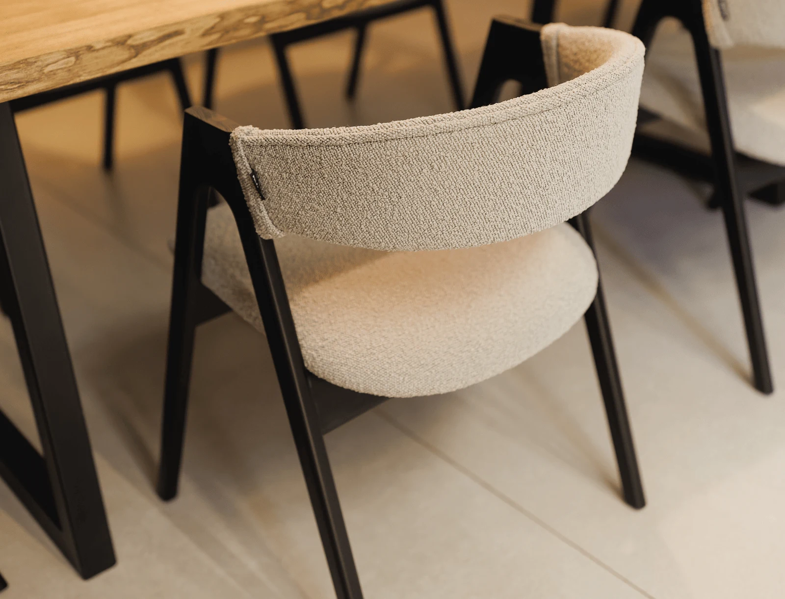 A cream boucle Lain chair on a black-stained ash frame pulled up at a light wood dining table with a console mirror behind