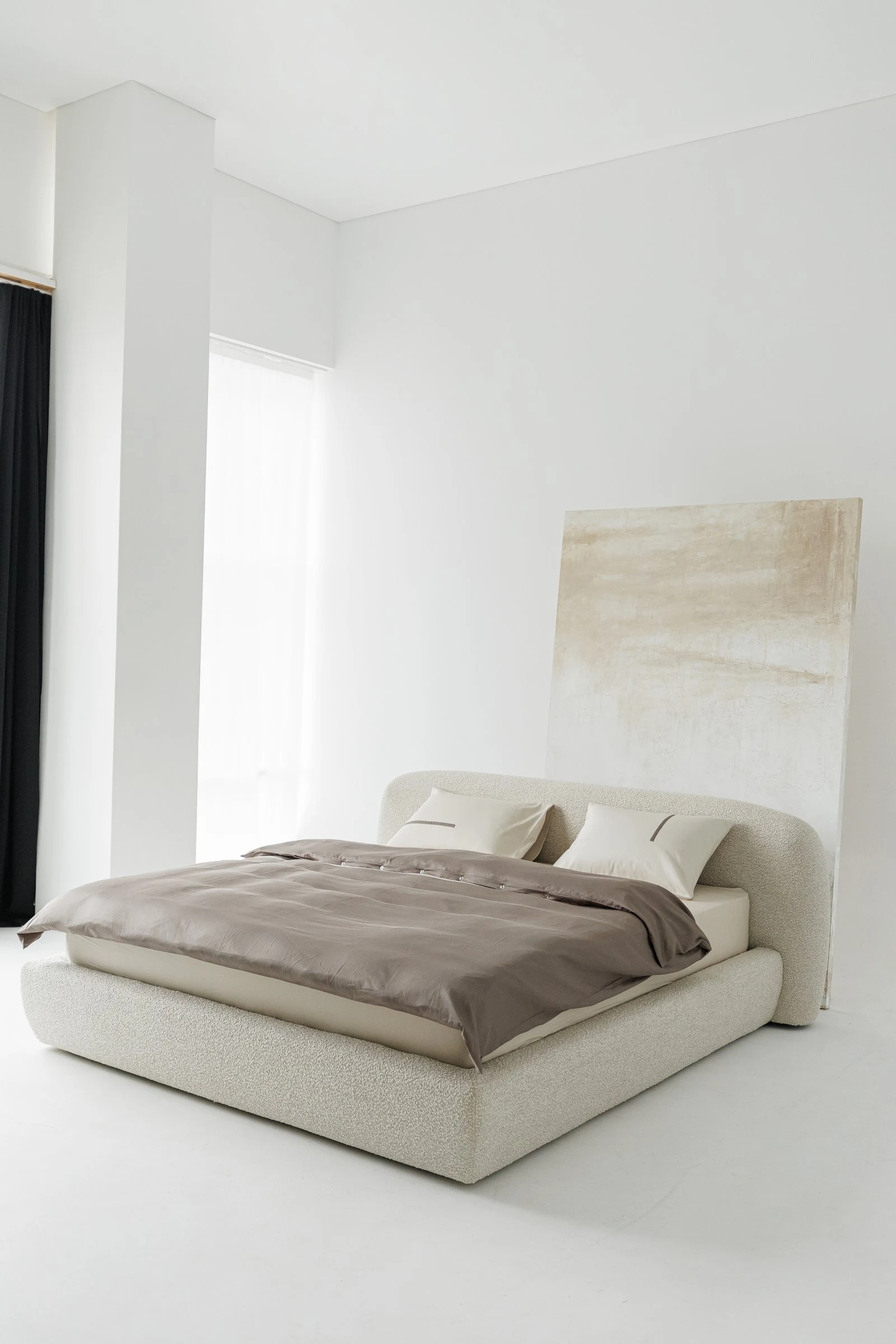 Cream boucle Belagio in a white studio with a painted canvas leaned behind the headboard, dark curtain at the edge