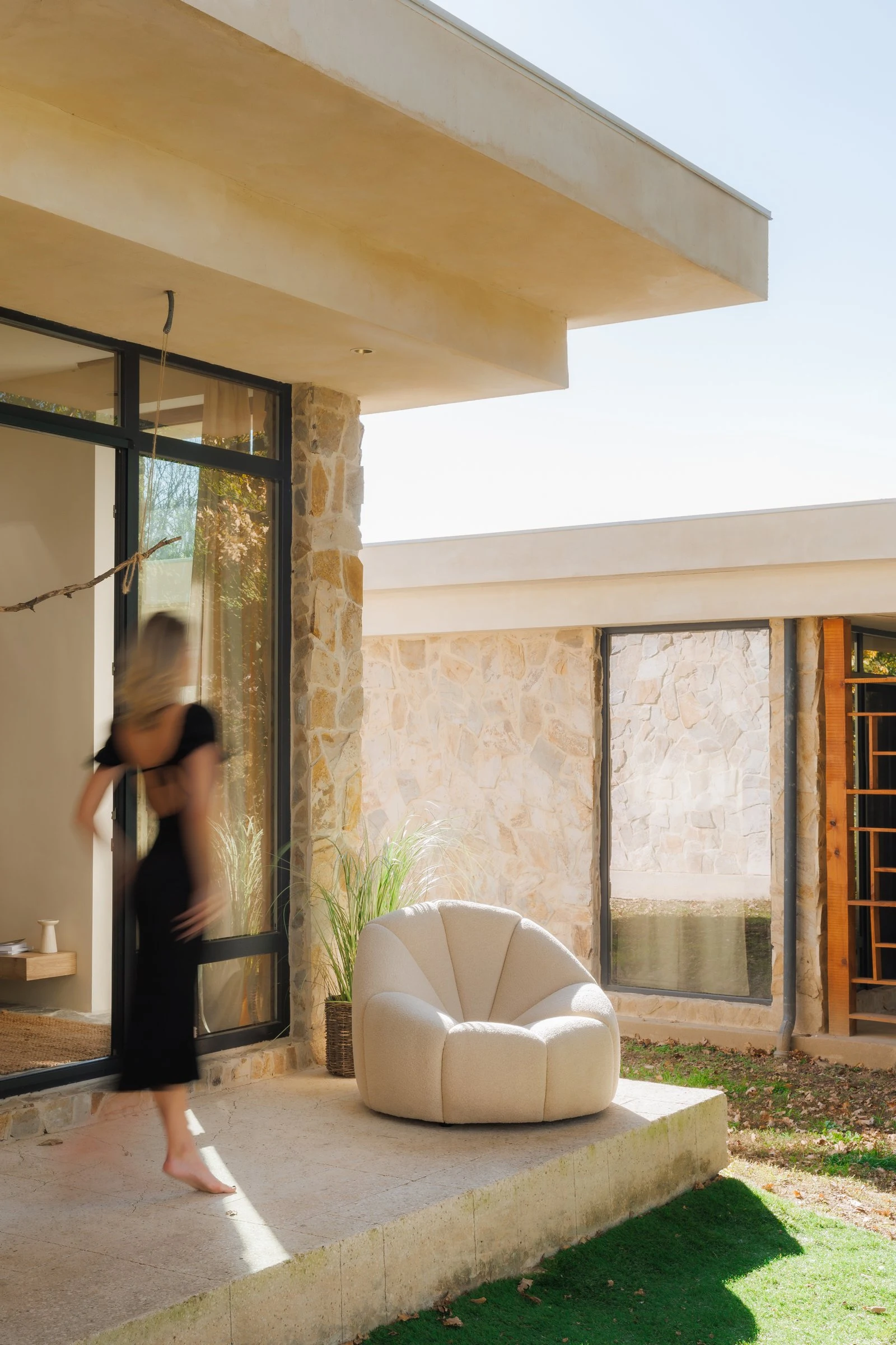 Three-quarter view of the cream boucle Flora chair on the stone villa patio with autumn trees beyond