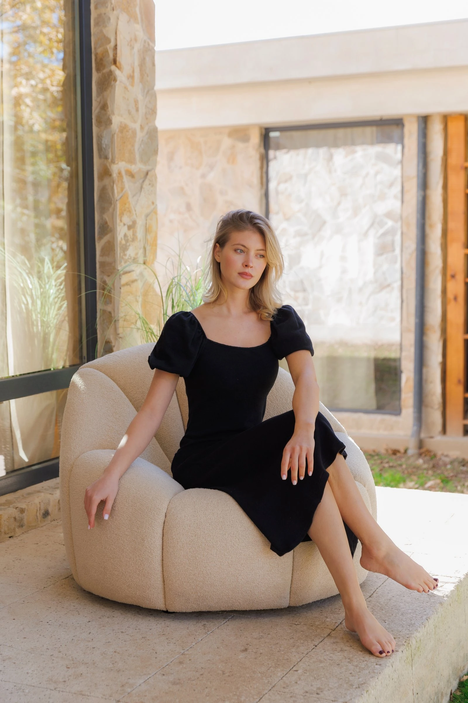 Model in a black dress seated on the Flora chair on the villa patio