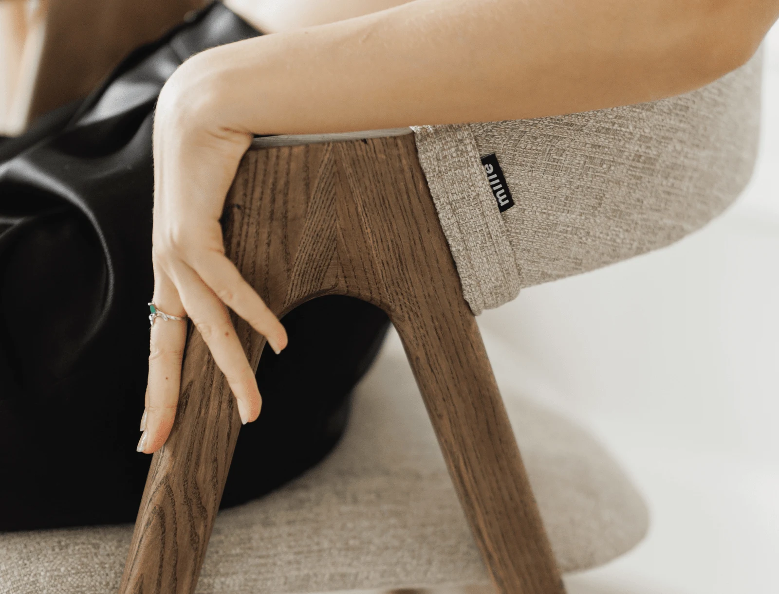 Close detail of the small Mille label sewn into the seam of a grey Lain chair, with a hand resting on the ash leg