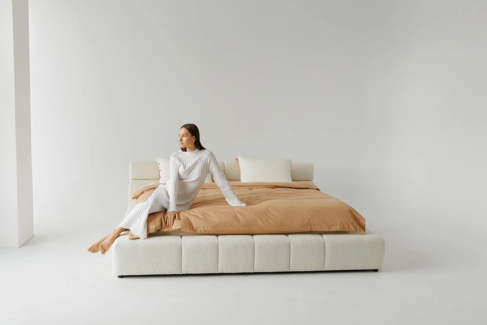 Cream boucle Nao with a model seated at the foot of the bed, white striped robe