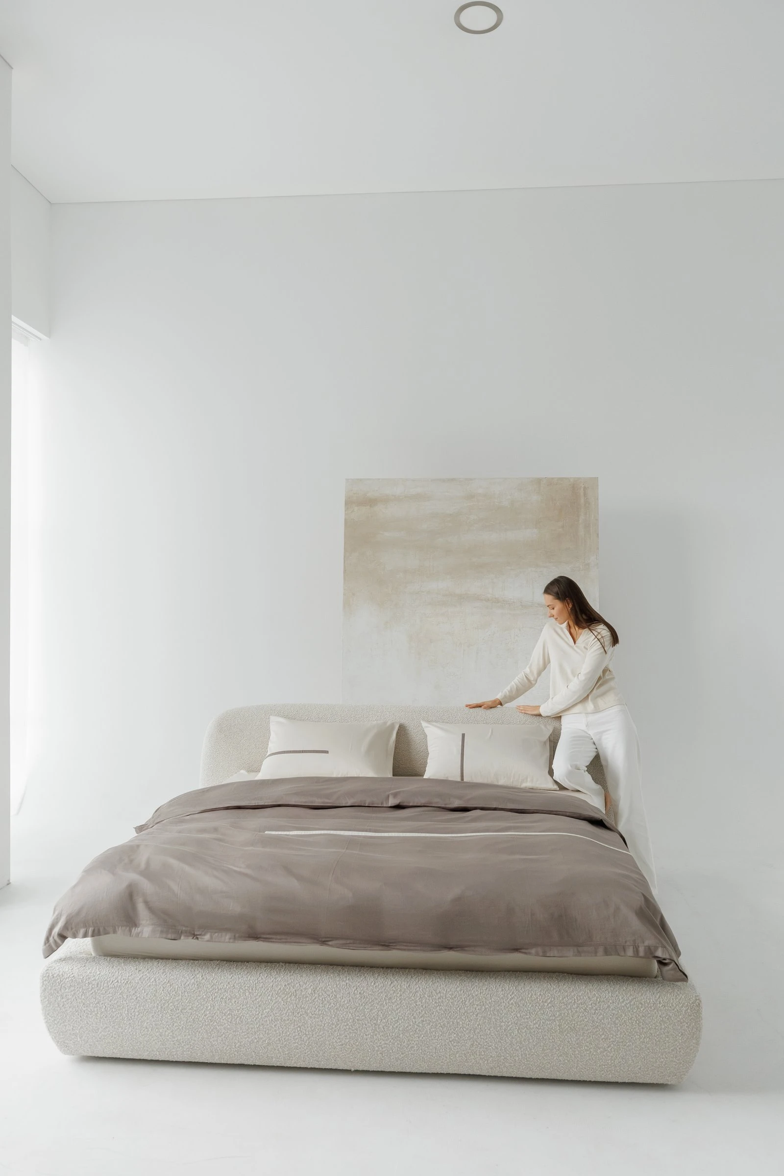 Cream boucle Belagio with a model in cream loungewear tucking a brown linen sheet across the bed