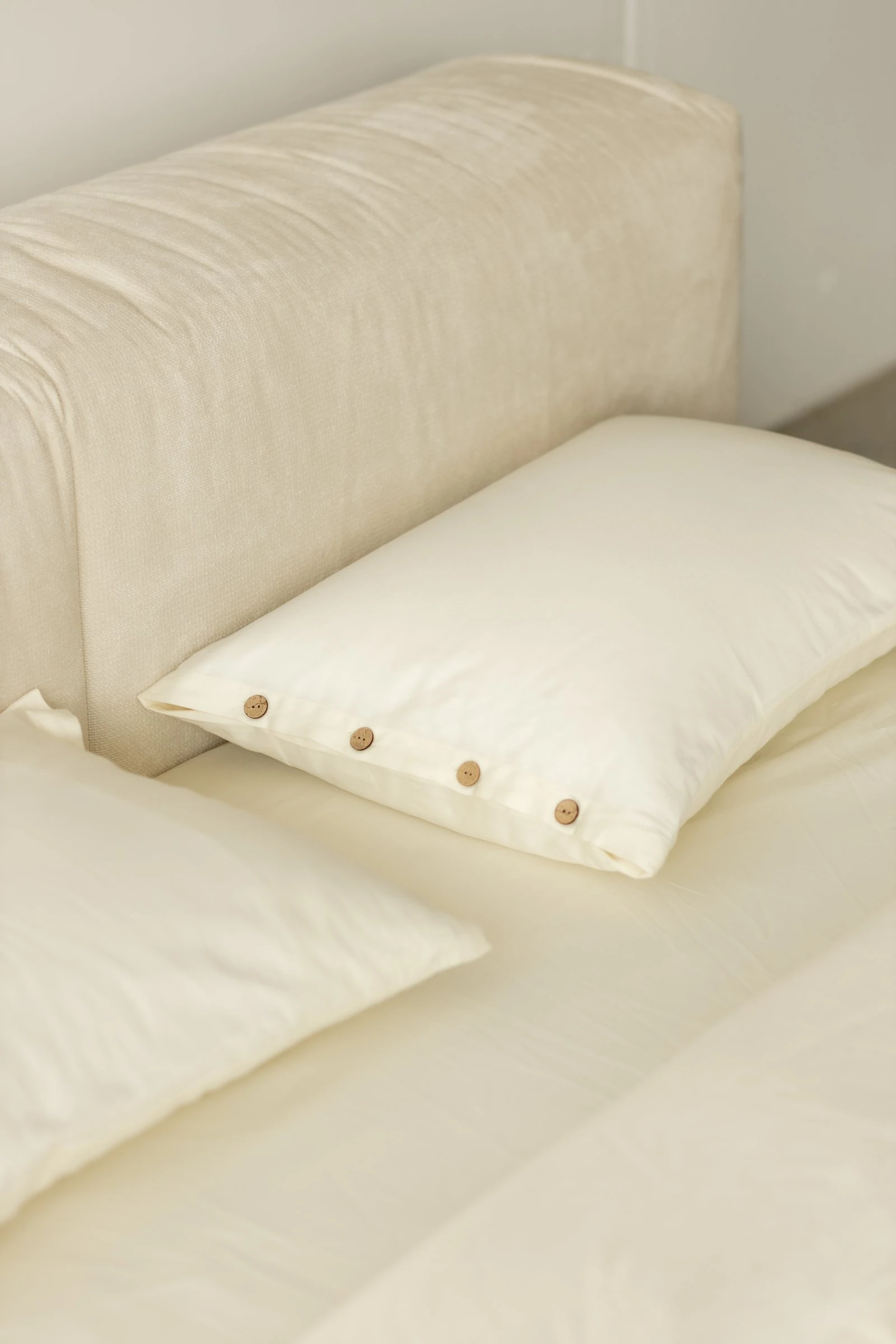 Two white pillows with a coconut-button row in front of the cream Marmaris slouchy headboard