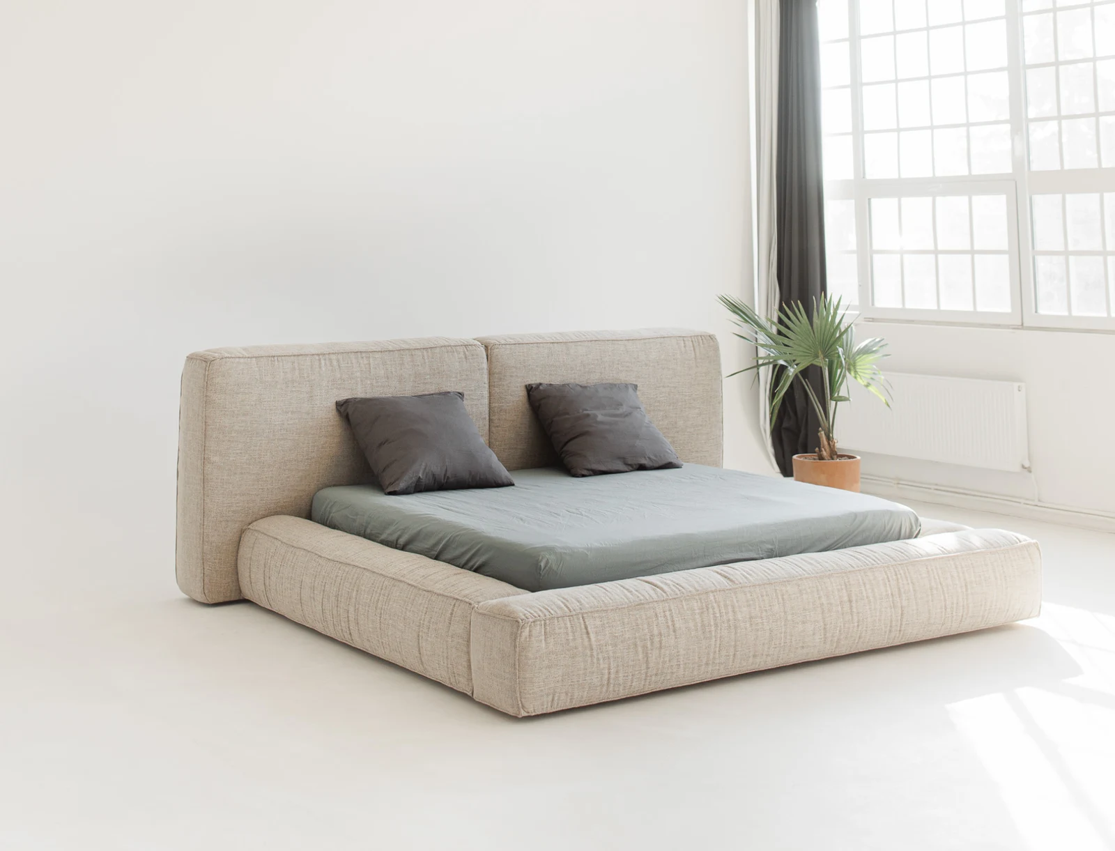 Sand-fabric Palermo in a bright minimal studio with a plant by the window, two grey pillows on the bed