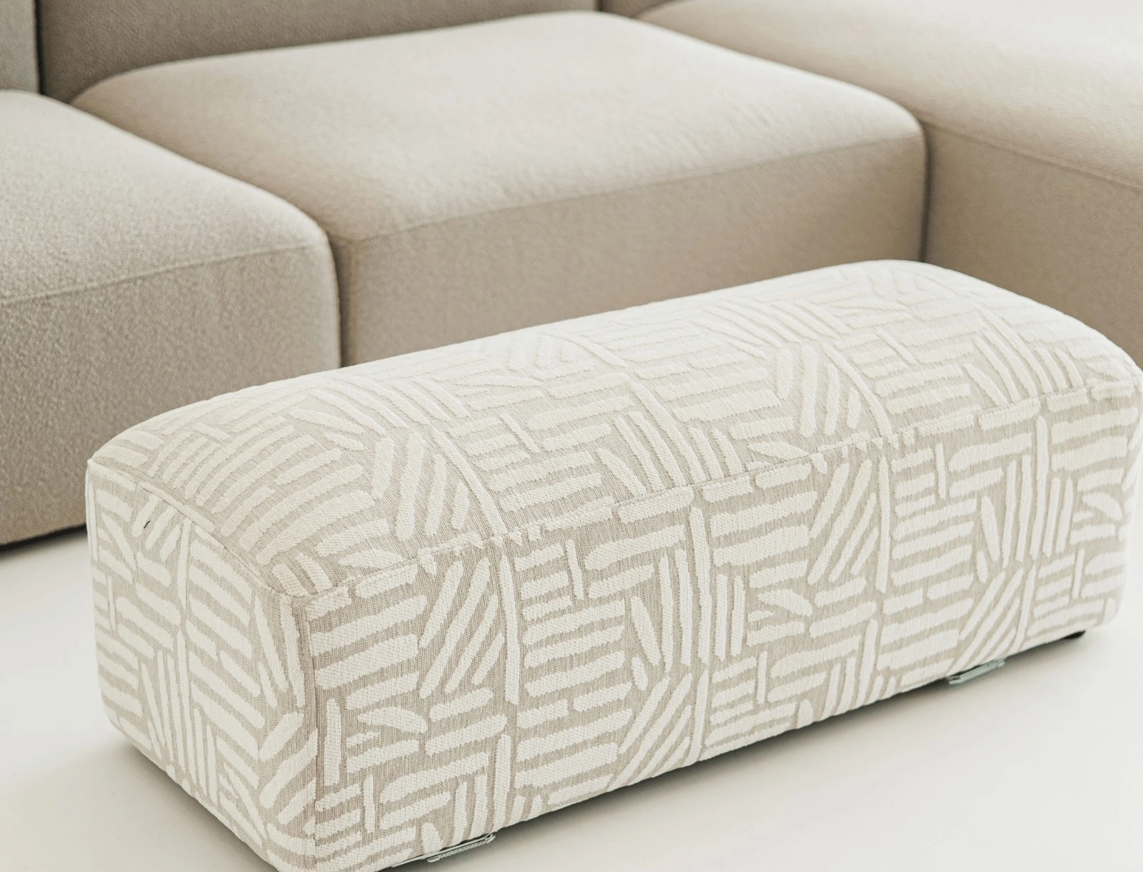Close detail of a patterned boucle Kingston pouf beside the cream sectional modules