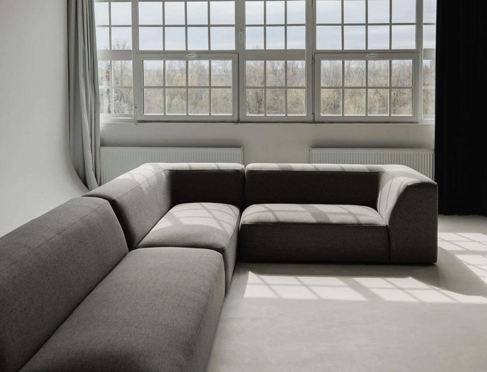 Charcoal Kingston sectional in an industrial loft with grid-paned windows and dappled sunlight