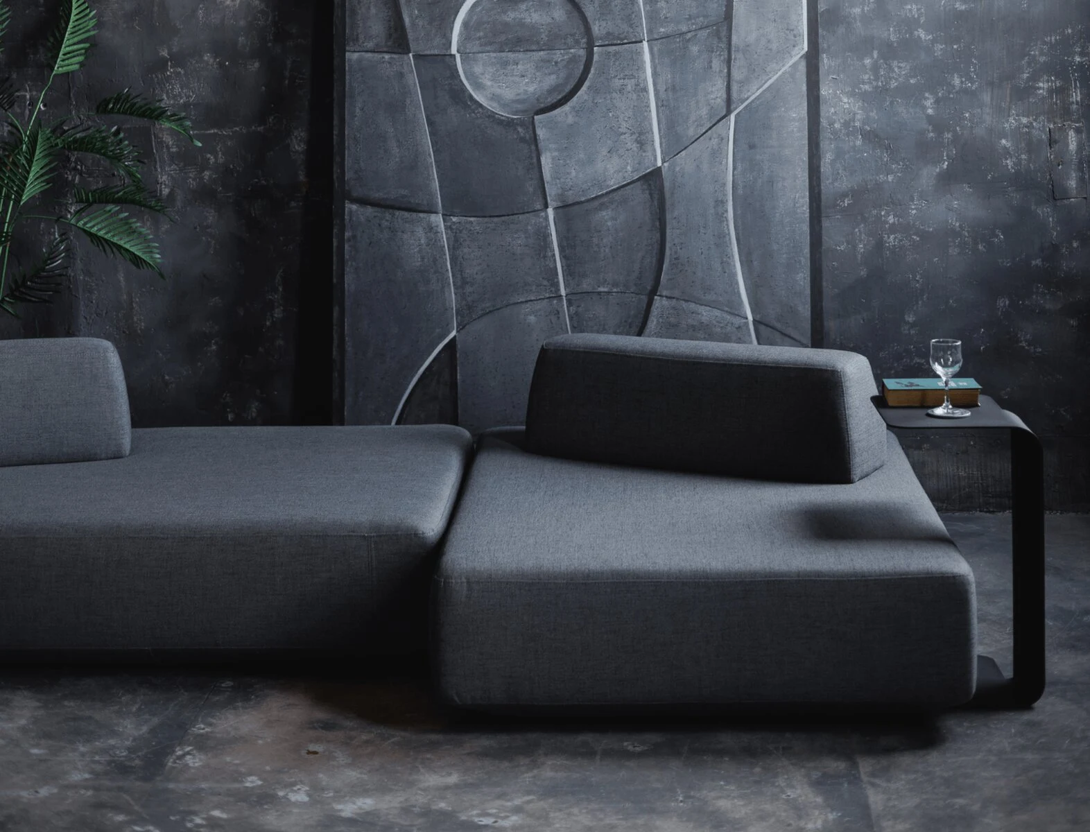 Charcoal Deseda in a dark concrete room with a tall industrial window and a leaning art panel