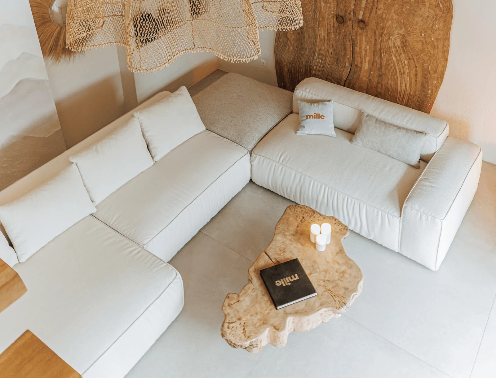 Overhead view of a cream Milano L-shape with a Mille pillow and a Mille book on a burl side table
