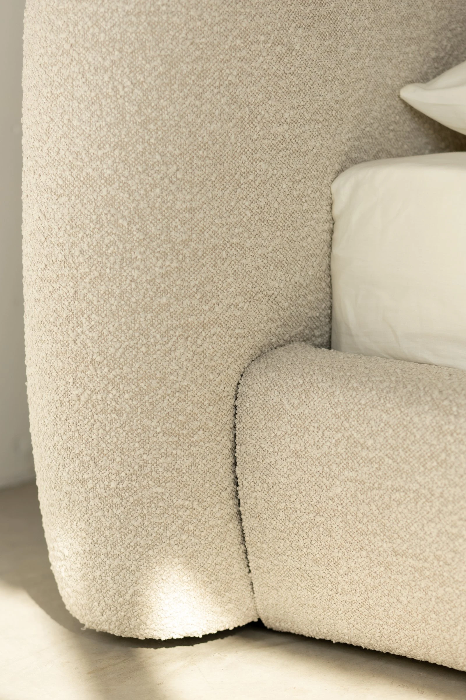 Macro of the Belagio cream boucle headboard curving down at the corner, soft daylight raking across the weave