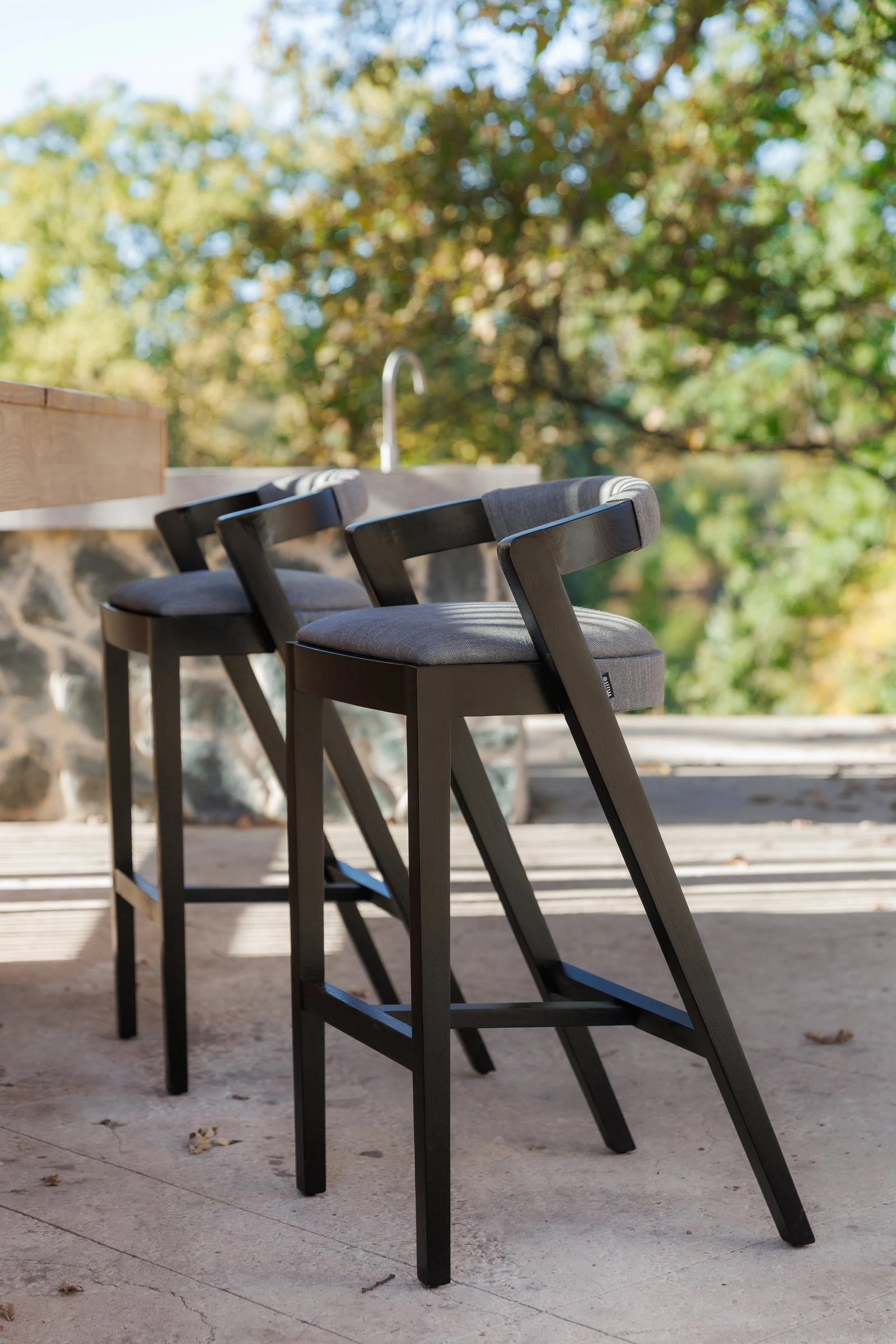 Two Baffi bar stools at an outdoor stone counter with autumn trees behind