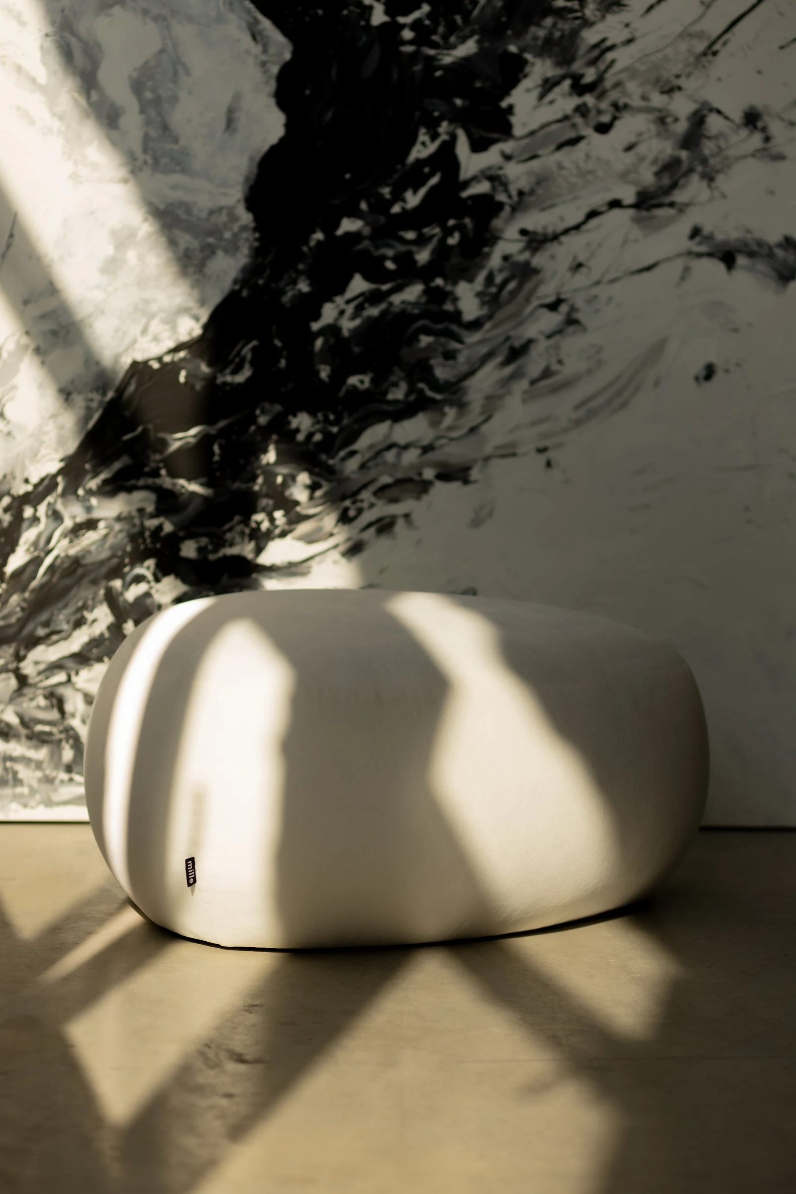 Cream velvet Chios pebble pouf against a marble wall with dramatic linear shadows