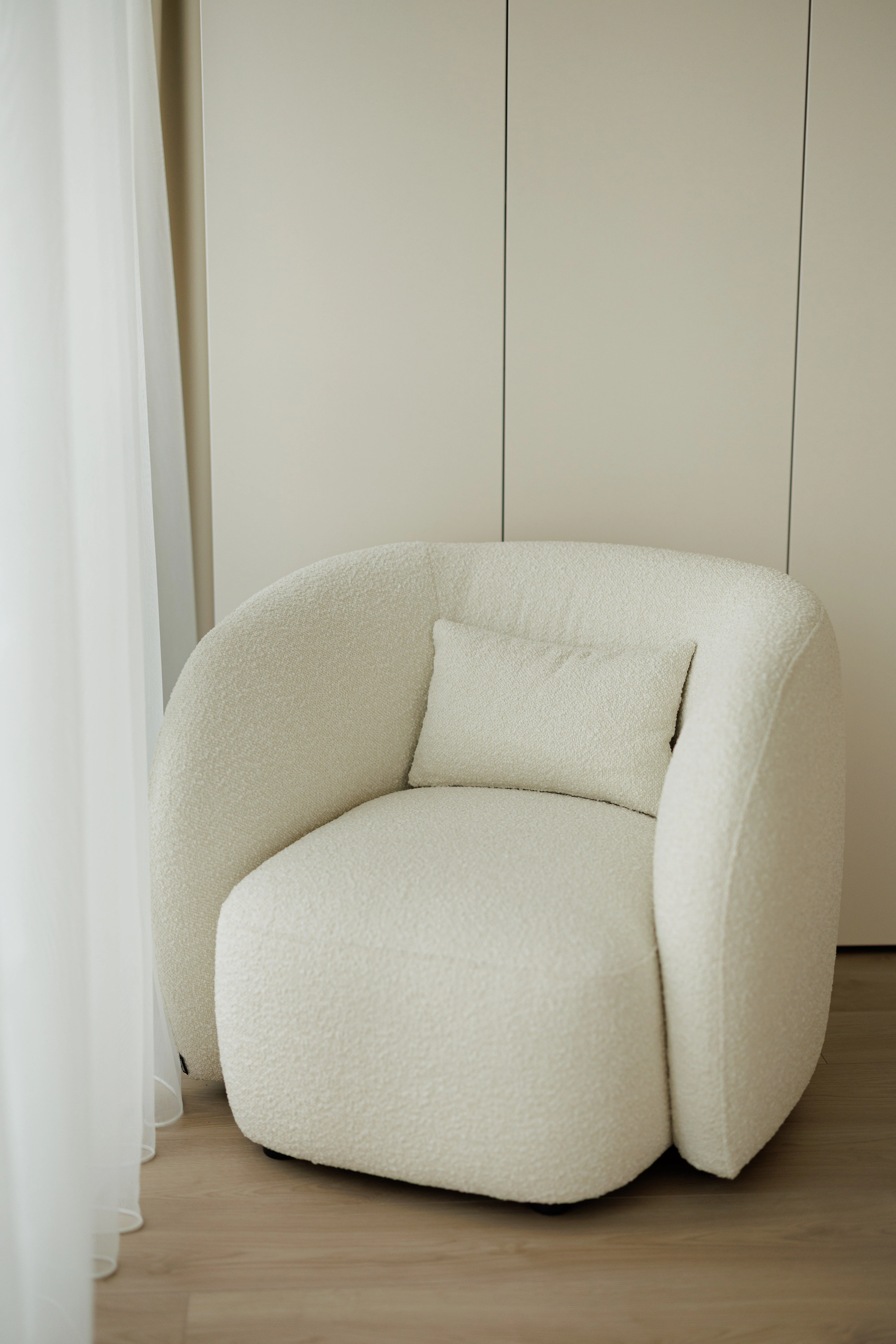 Cream boucle Nuba armchair in an apartment by a sheer white curtain with pale wall and oak floor