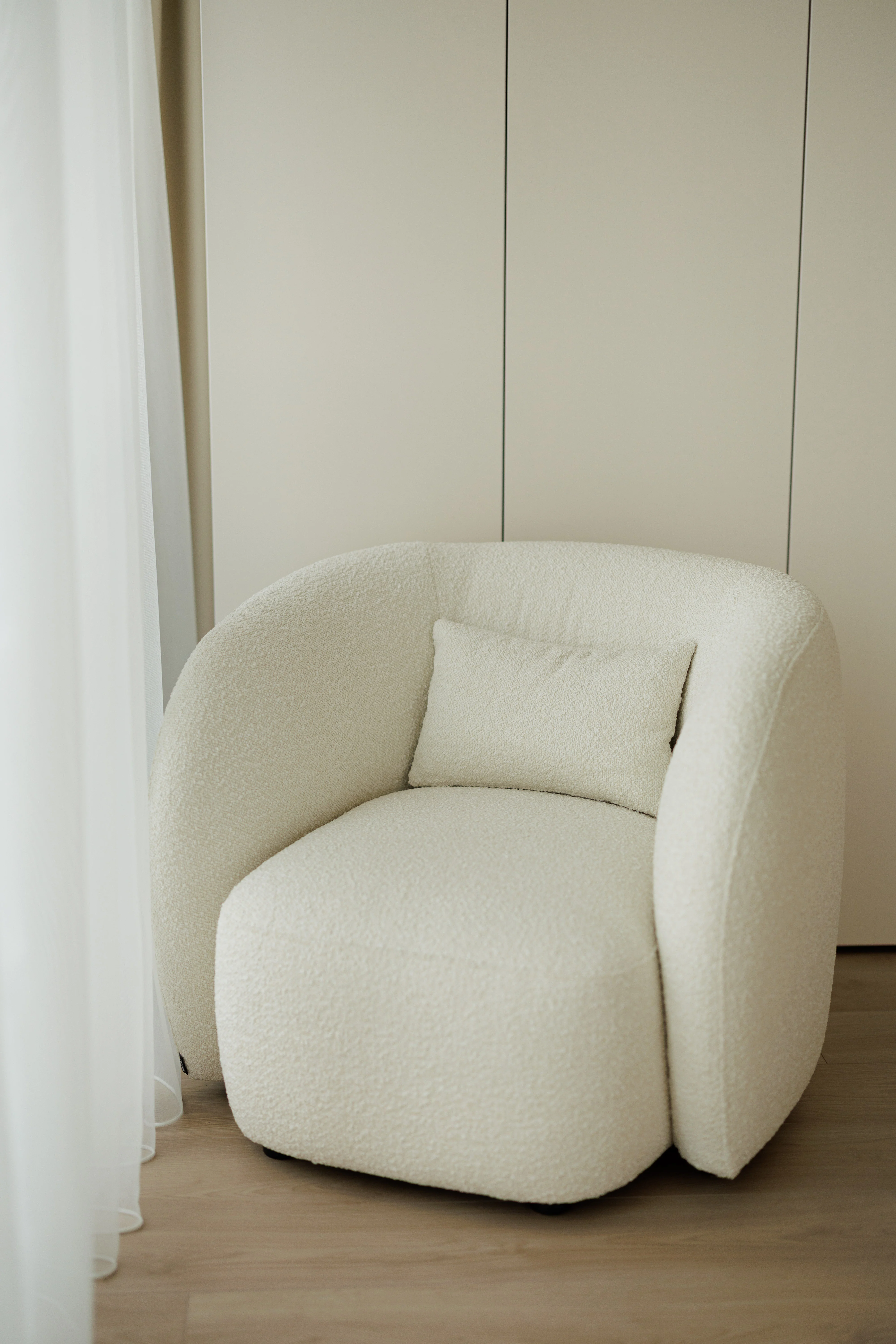 Cream boucle Nuba armchair in an apartment by a sheer white curtain with pale wall and oak floor