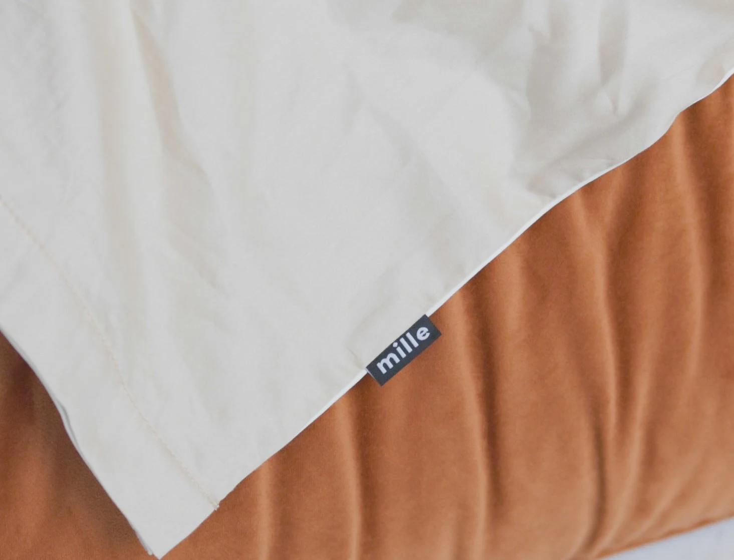 Close detail of the small Mille label sewn into the seam of a burnt-orange velvet Palermo with white sheets