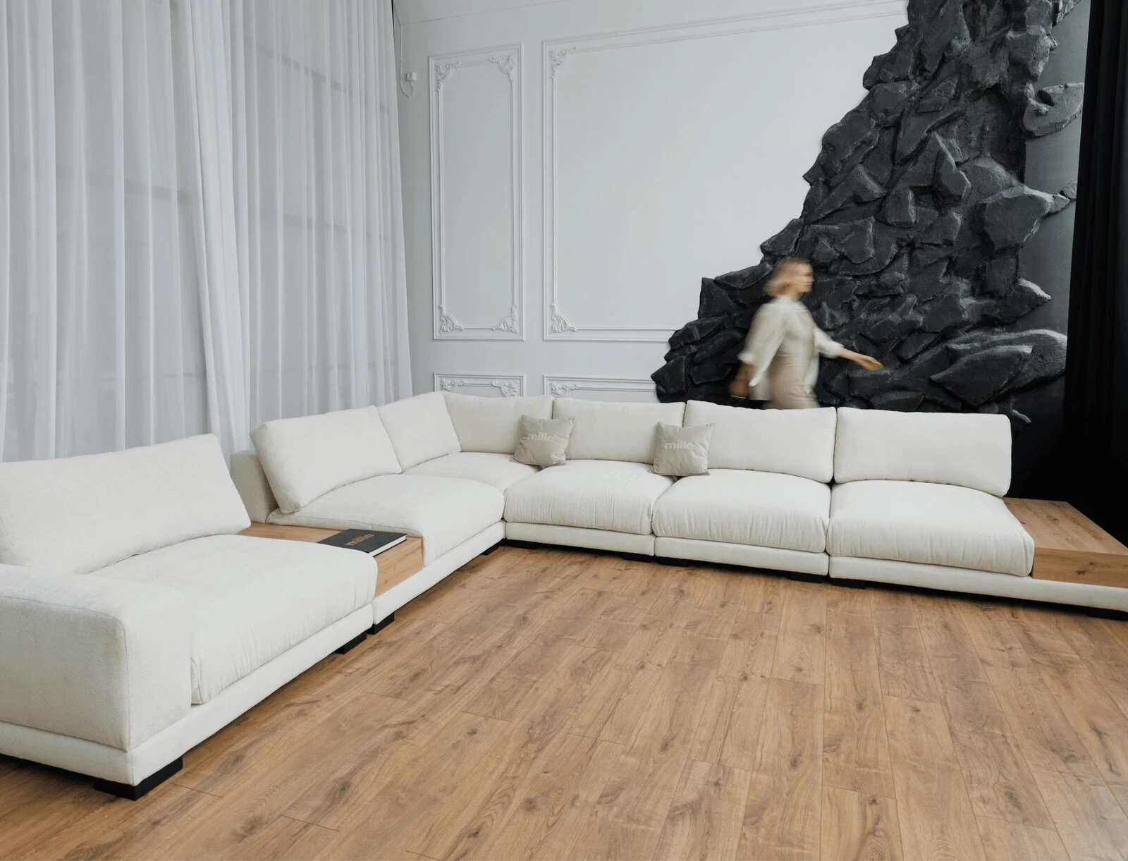Cream Palermo sectional against a stone-art wall with a figure walking past in motion blur