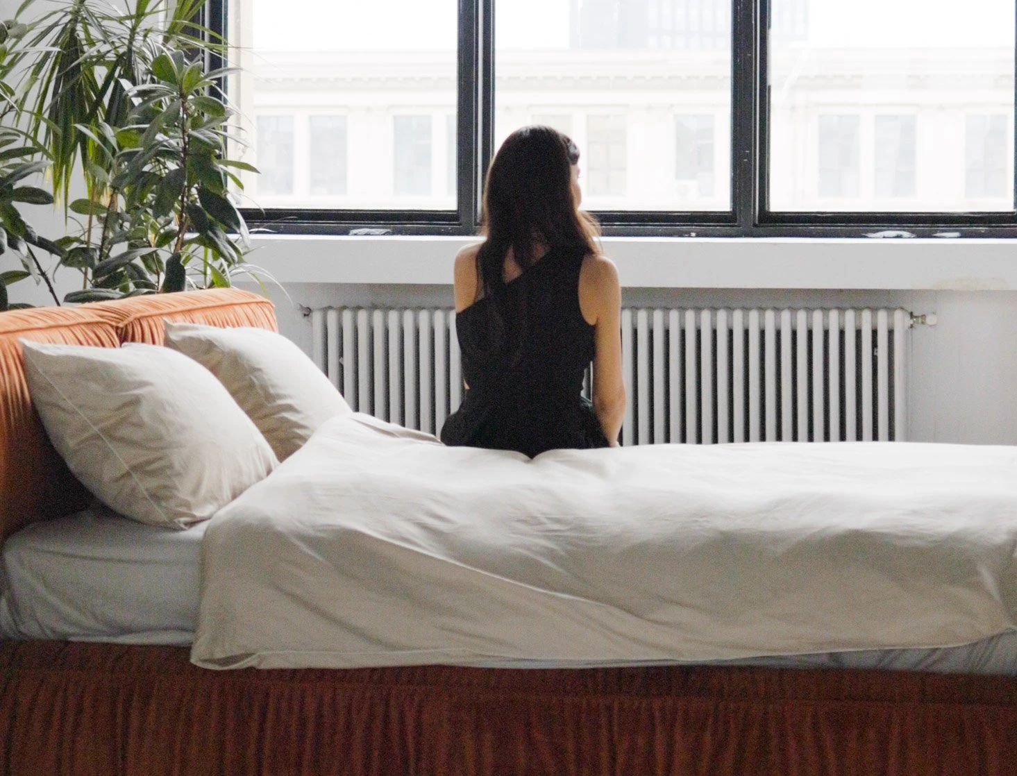 Model seated on a burnt-orange velvet Palermo, facing a window in an industrial loft