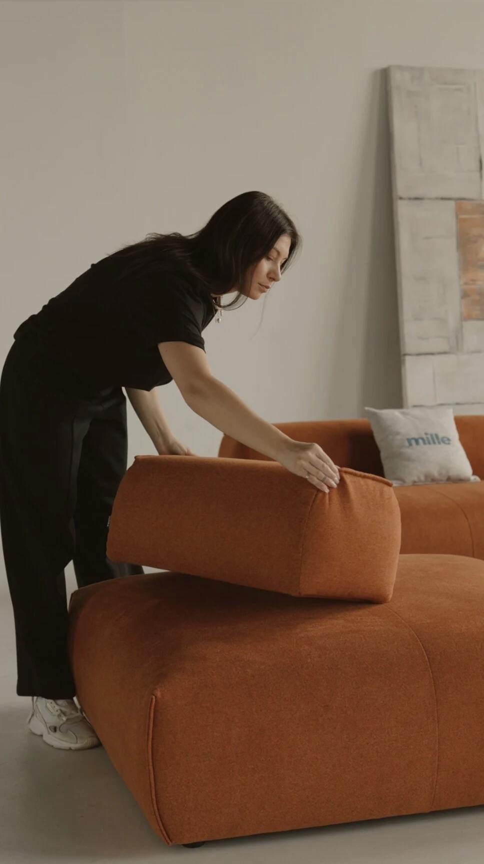 Model in black lifting the rust Nissa backrest module to demonstrate the moveable cushion system