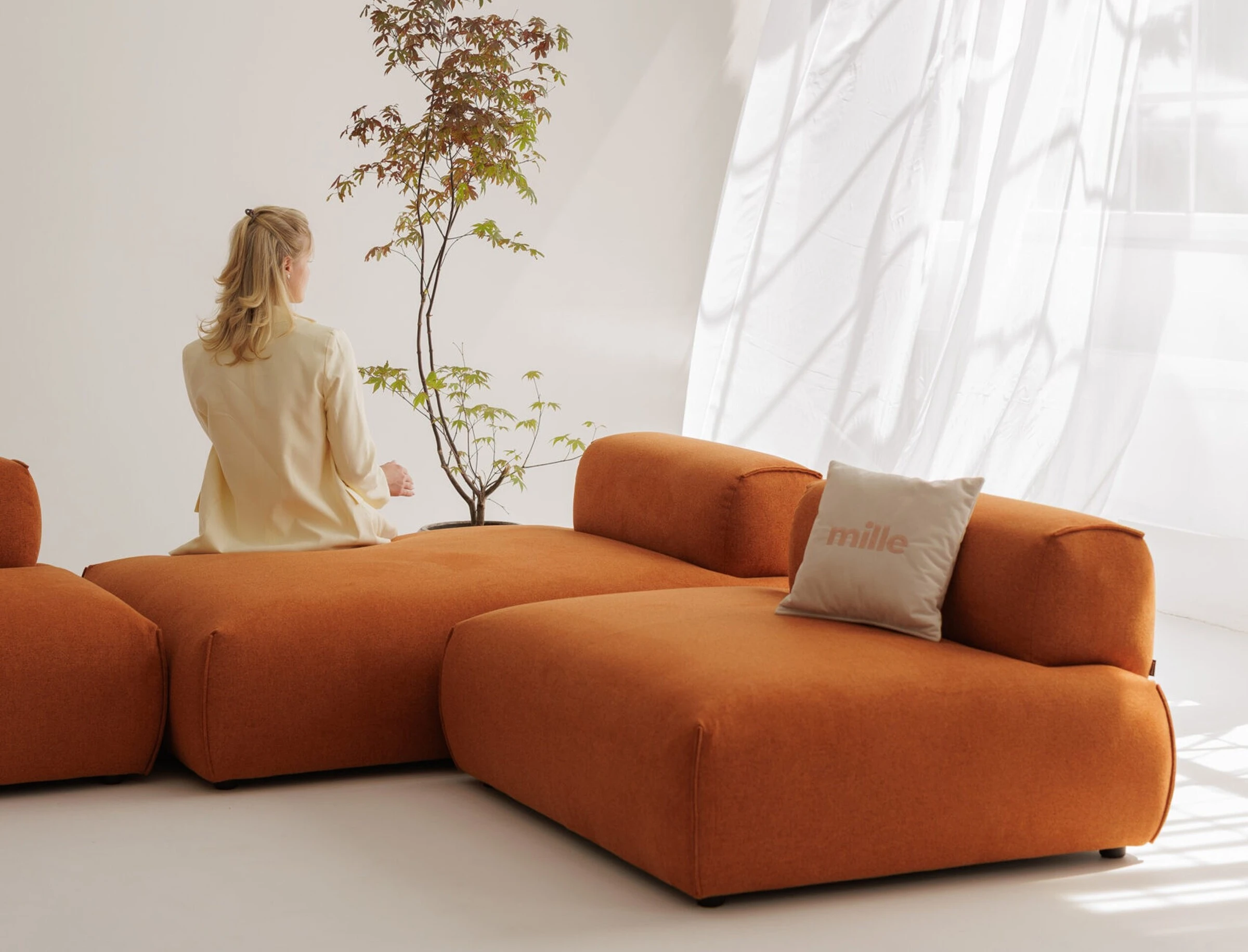 Model catching a Mille pillow on the rust Nissa modular in the white studio
