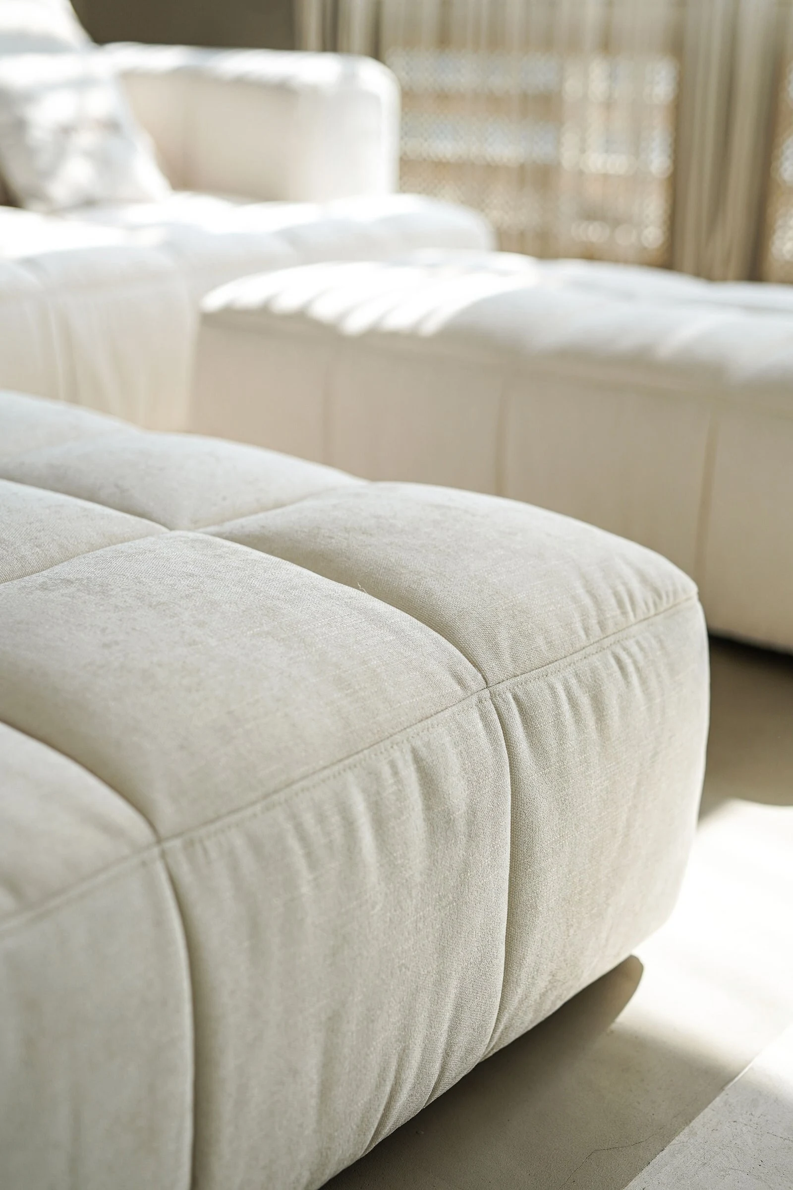 Macro detail of cream tufted Soft cushions with golden sunbeams across the seams