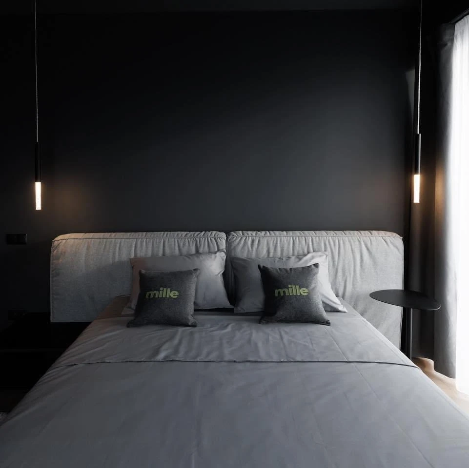 Mid-grey Palermo photographed dead-centered in a dark bedroom with Mille-branded pillows on the bed and tube pendants either side