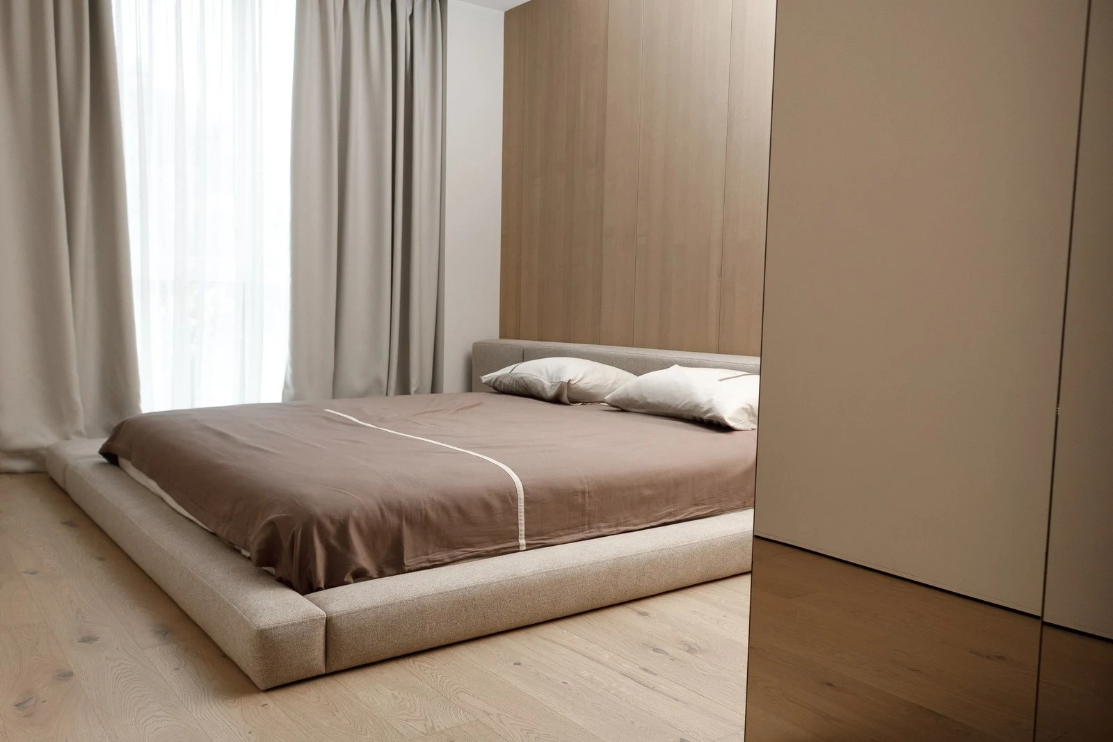 Sand Connect bed in a wood-paneled bedroom with the L-shape bench extension on the right and a brown sateen duvet draped across the bed